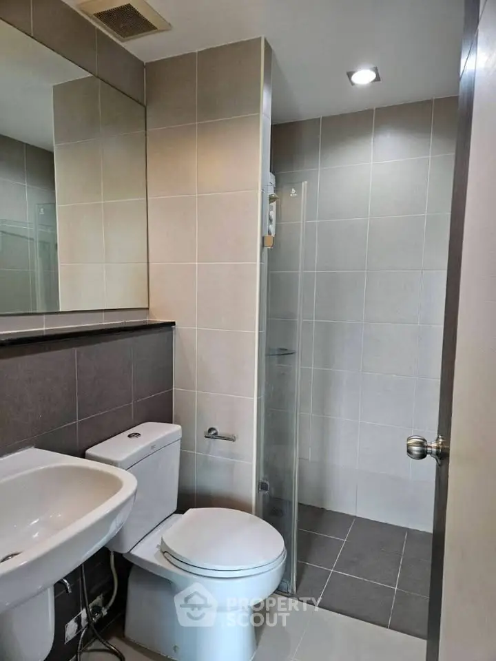 Modern bathroom with sleek design and neutral tiles, featuring a glass shower enclosure and contemporary fixtures.