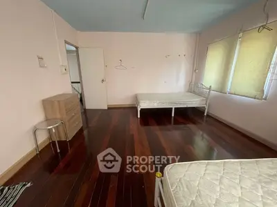 Spacious bedroom with wooden flooring and natural light, featuring two beds and a dresser.