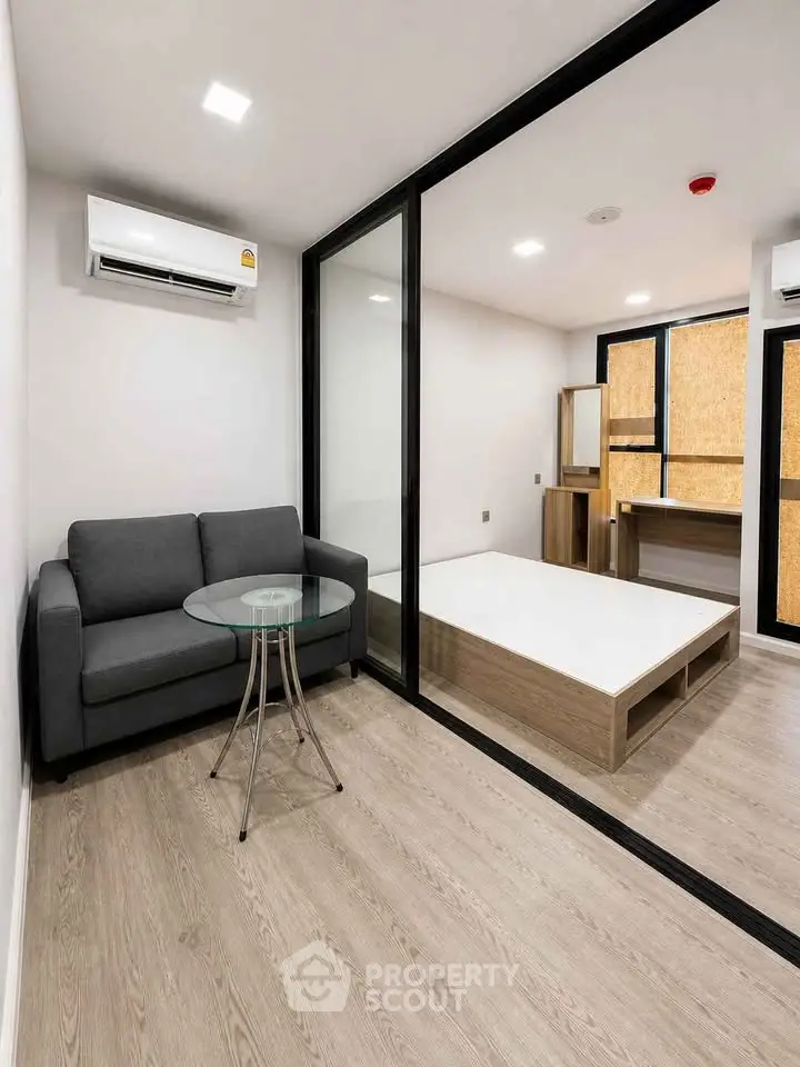 Modern studio apartment with sleek design, featuring a cozy living area and stylish bedroom separated by glass partition.