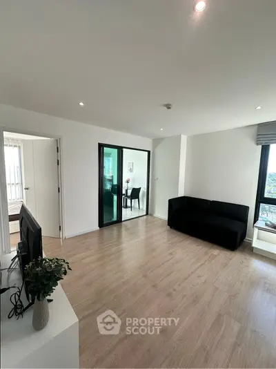 Spacious modern living room with sleek black sofa and large windows offering natural light.