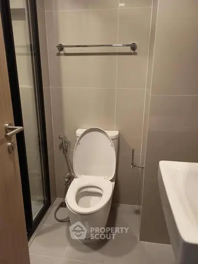 Modern bathroom with sleek fixtures and neutral tiles, featuring a toilet and a glass shower door.