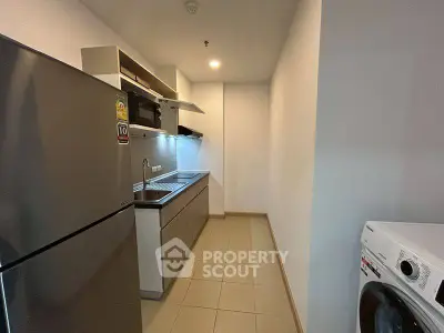 Modern kitchen with stainless steel appliances and washing machine in sleek apartment.