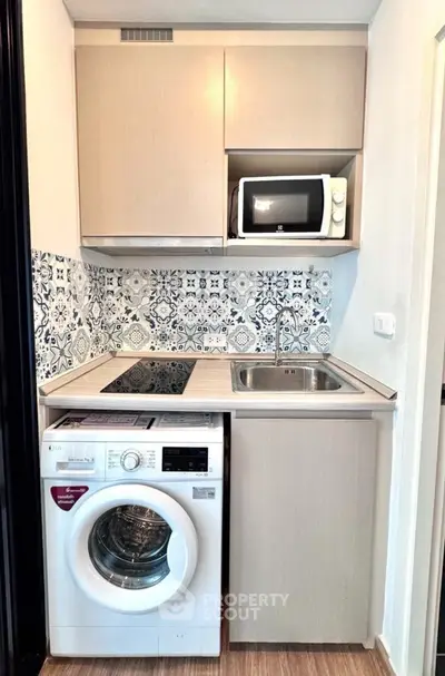 Compact modern kitchen with washing machine, microwave, and stylish backsplash tiles.