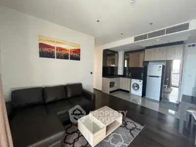Modern living room with sleek kitchen, featuring black leather sofa and contemporary appliances.