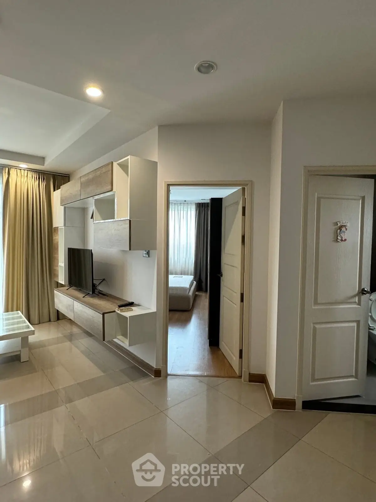 Modern living room with sleek furniture and open doorway to bedroom, featuring natural light and elegant design.