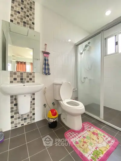 Modern bathroom with glass shower, white tiles, and colorful accents in a contemporary home.