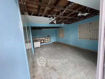 Spacious room with blue walls and tiled floor, featuring large windows and exposed ceiling.