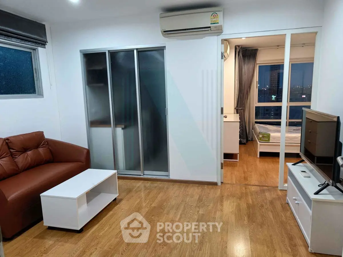 Modern apartment living room with wooden flooring, sliding glass doors, and cozy furniture.