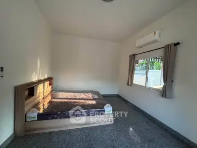 Spacious bedroom with modern bed and air conditioning, featuring large window for natural light.