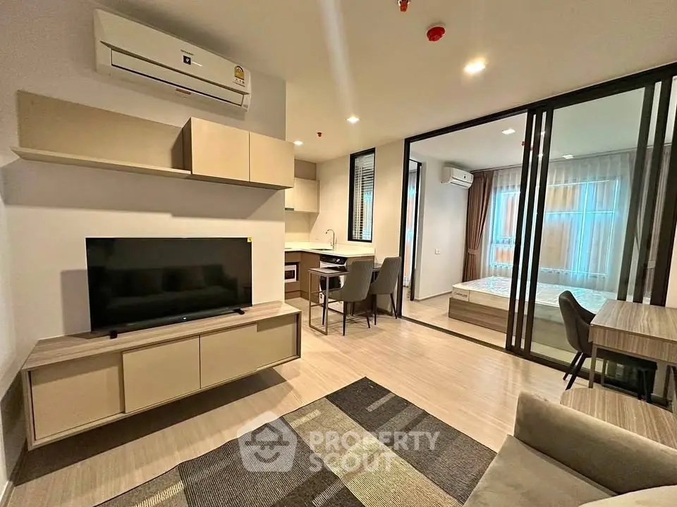 Modern open-plan living room with sleek furniture and glass partition to bedroom