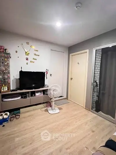 Cozy living room with modern decor and wall clock, featuring a TV and fan on wooden flooring.