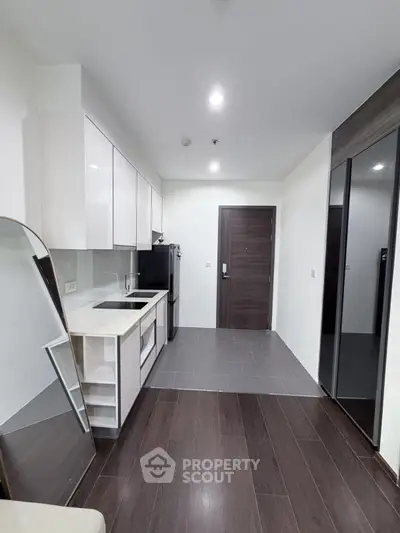 Modern kitchen with sleek cabinetry and dark wood flooring, featuring a compact design.