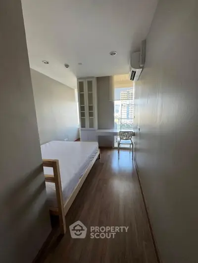 Cozy bedroom with wooden flooring and large window offering city views, perfect for urban living.