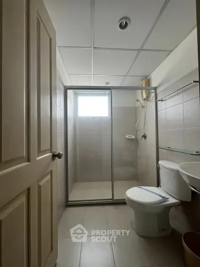 Modern bathroom with glass shower enclosure and tiled walls, featuring a sleek design and natural lighting.