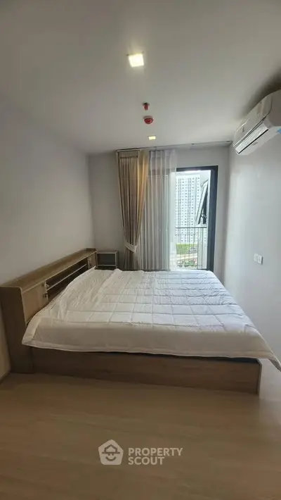 Modern bedroom with large window and city view, featuring a cozy bed and air conditioning.