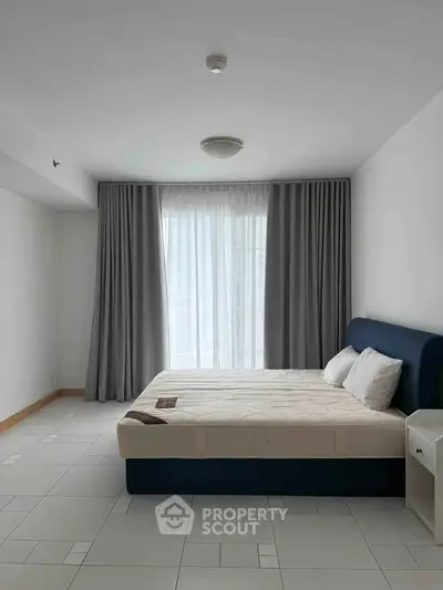 Spacious bedroom with large window and modern furnishings in a minimalist style.