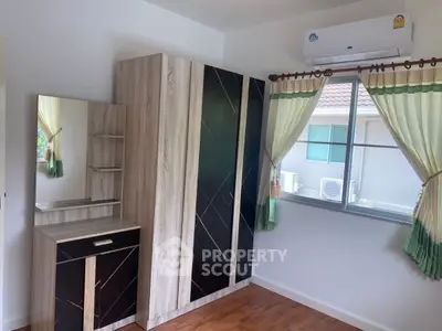 Cozy bedroom with modern wardrobe and air conditioning, featuring a window view of neighboring houses.
