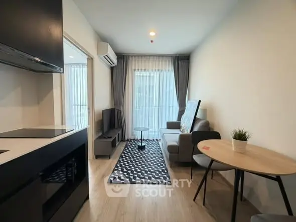 Modern living room with stylish decor and natural light, featuring a cozy seating area and sleek kitchen.