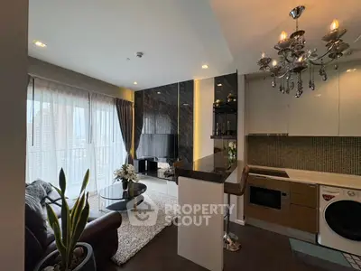 Luxurious modern living room with open kitchen, featuring elegant chandelier and large windows.