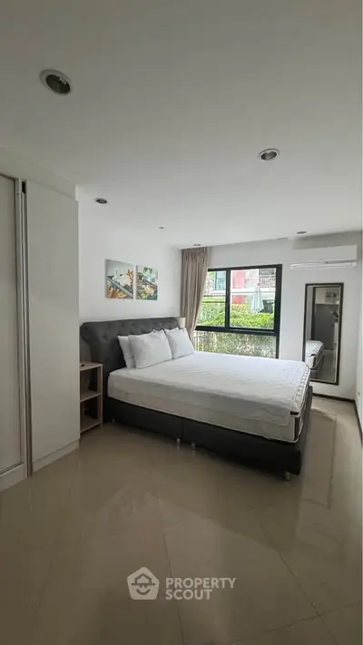 Spacious bedroom with modern decor and large window offering natural light.