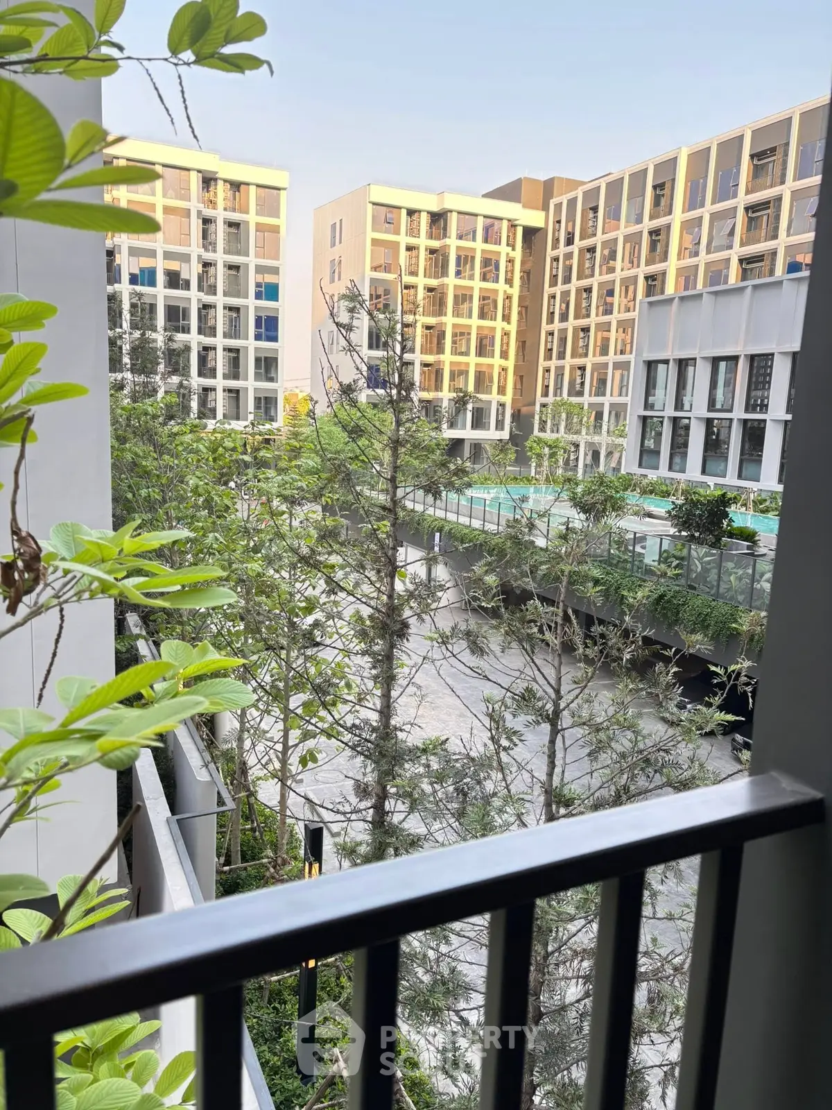 Modern apartment complex with lush greenery and pool view from balcony.