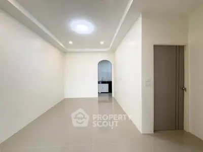 Spacious modern living room with sleek tile flooring and recessed lighting, leading to a kitchen area.