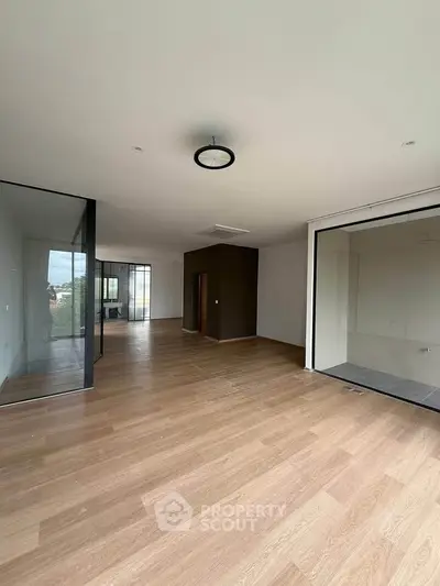 Spacious modern living room with wooden flooring and large windows offering natural light.