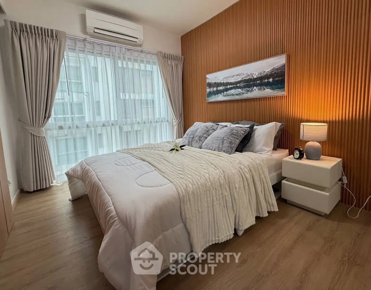 Elegant bedroom with cozy bedding, wooden accent wall, and large window with sheer curtains.