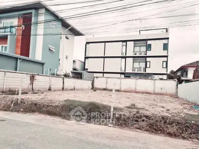 Vacant land plot in a residential area with modern houses nearby.
