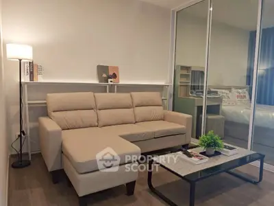 Modern living room with beige sofa and glass partition leading to bedroom, featuring stylish decor and cozy ambiance.