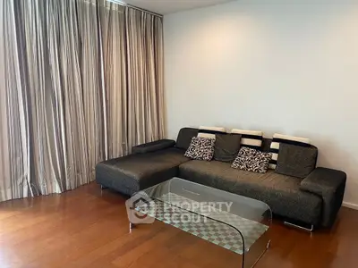 Modern living room with stylish sofa and glass coffee table on wooden floor.