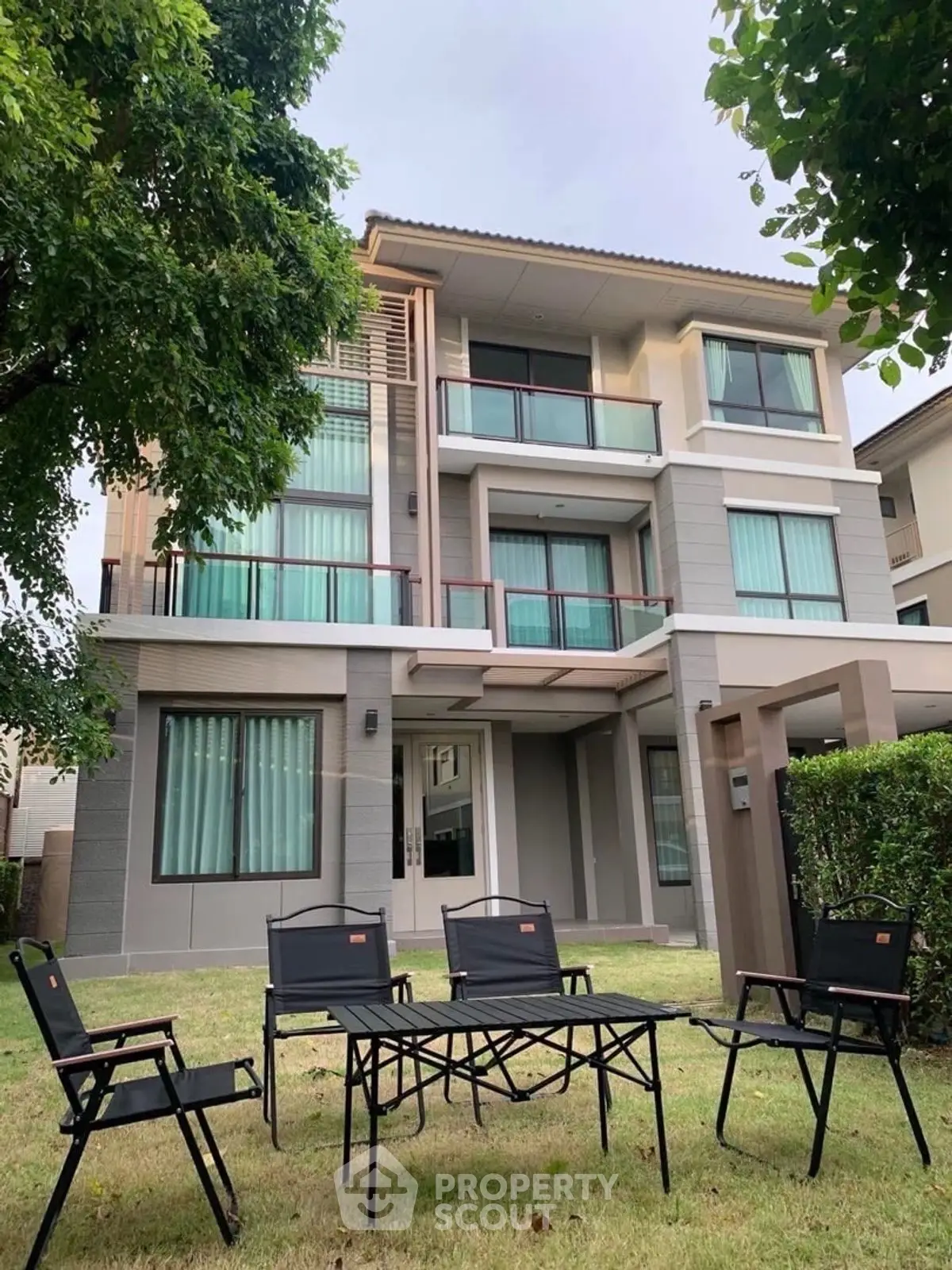Modern three-story house with spacious garden and outdoor seating area.
