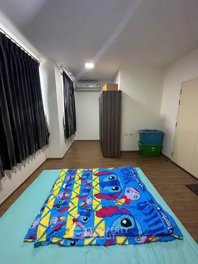 Spacious bedroom with colorful bedding and modern decor, featuring ample natural light and sleek flooring.
