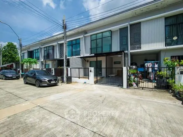 Modern townhouse exterior with driveway and parked cars in a suburban neighborhood.