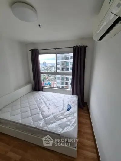 Modern bedroom with large window offering city view, featuring a new mattress and air conditioning.