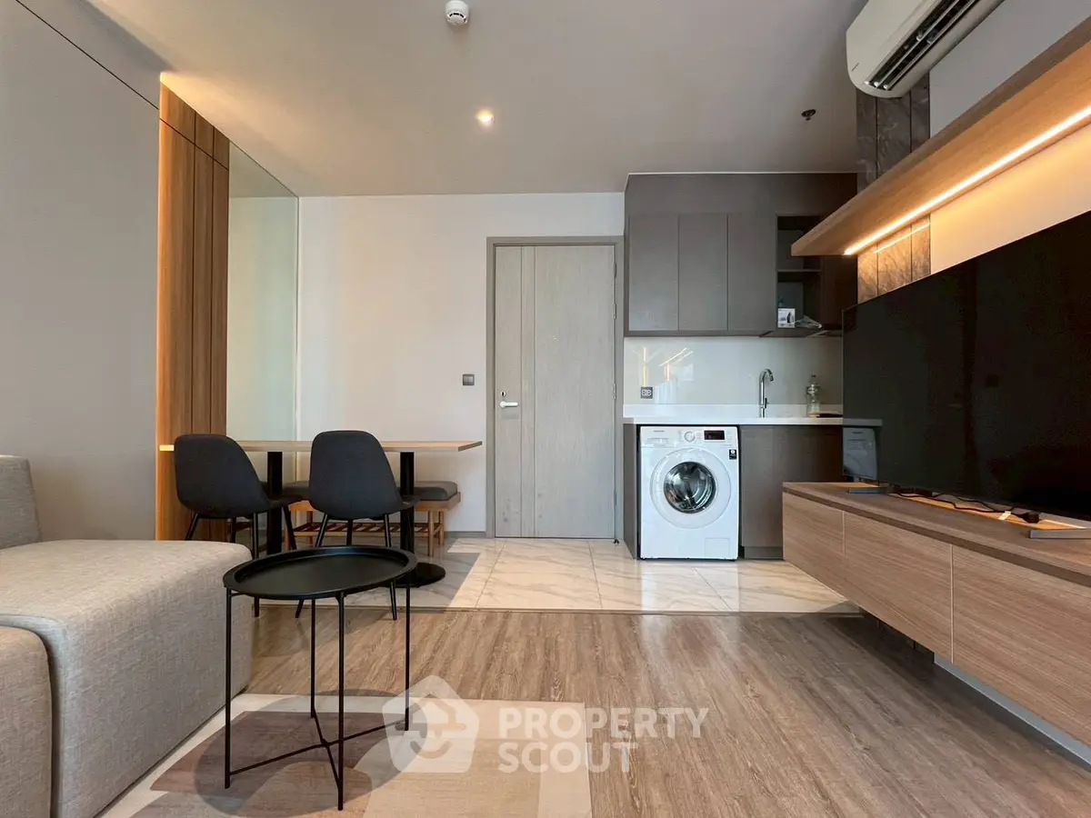 Modern living room with sleek furniture and built-in kitchen appliances, featuring a washing machine and stylish decor.