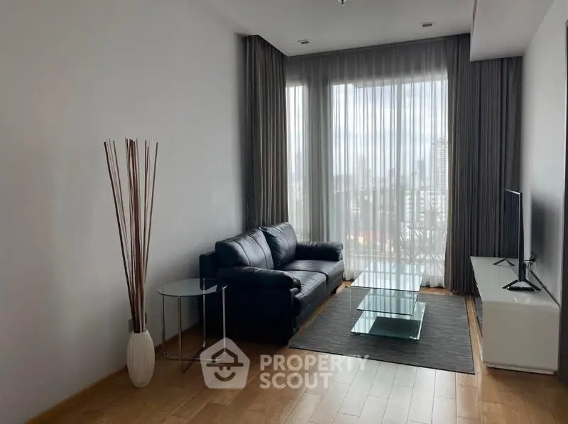 Modern living room with sleek black sofa, glass coffee table, and floor-to-ceiling windows offering city views.