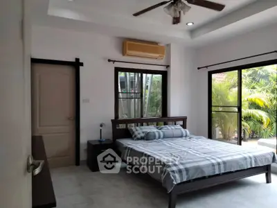 Spacious bedroom with large windows and garden view, featuring modern decor and ceiling fan.