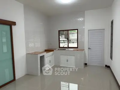 Modern kitchen with sleek white tiles and wooden accents, featuring a large window for natural light.