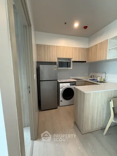 Modern kitchen with wood cabinets, fridge, and washing machine in compact layout.