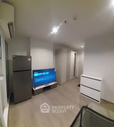 Modern living room with sleek design, featuring a flat-screen TV and stainless steel refrigerator.