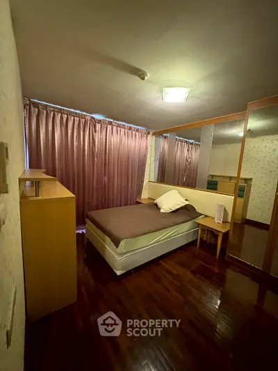 Cozy bedroom with wooden flooring and large mirror reflecting natural light