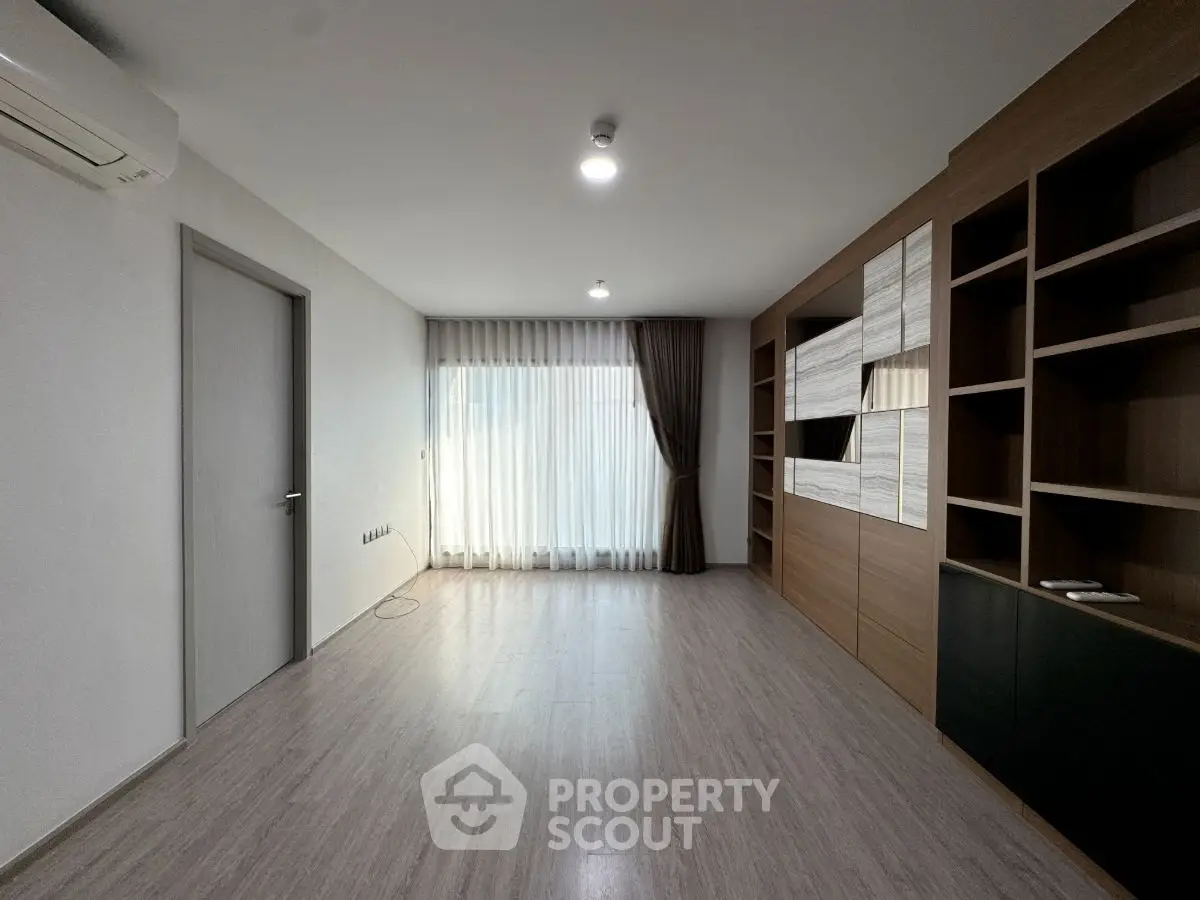 Spacious modern living room with built-in shelving and large window for natural light.