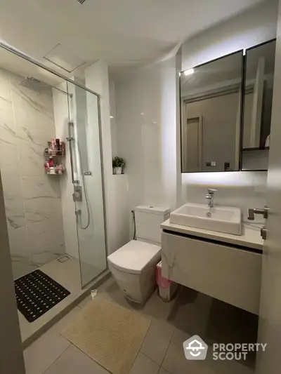 Modern bathroom with glass shower and sleek vanity in contemporary apartment.