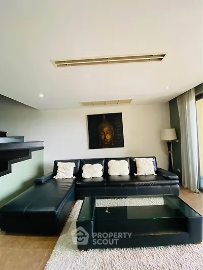 Spacious living room with modern black leather sofa and glass coffee table, featuring elegant decor and ambient lighting.