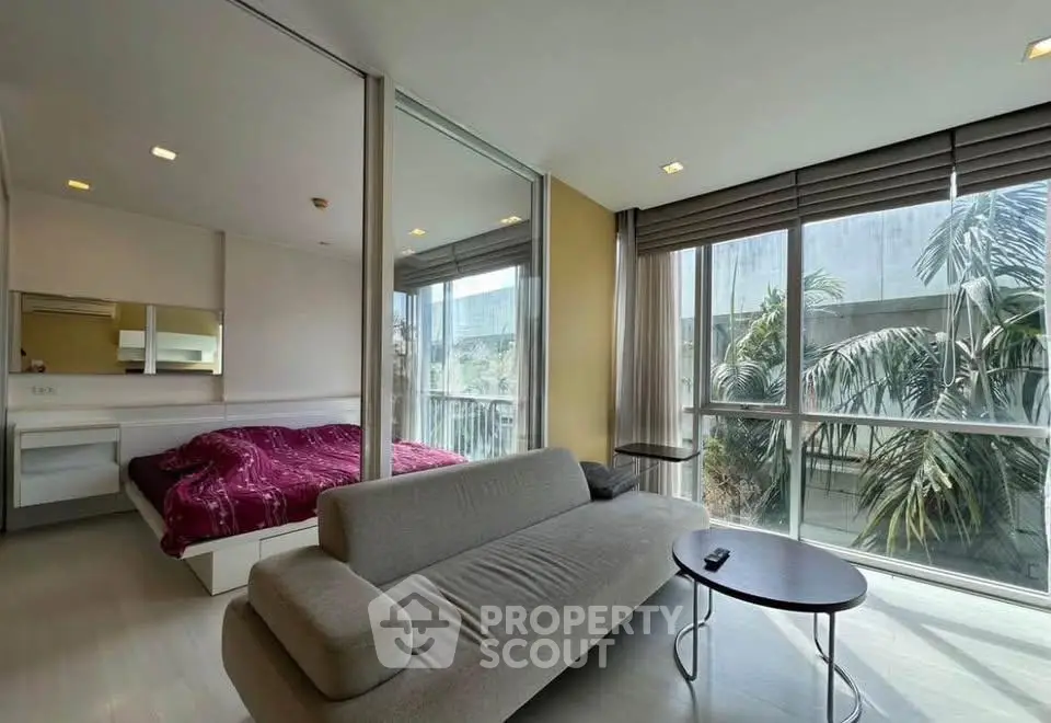 Modern living room with large windows and cozy sofa, featuring a view of lush greenery.