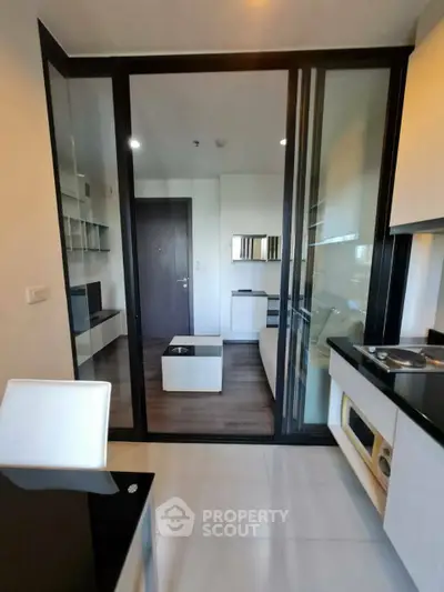 Modern apartment with sleek kitchen and cozy living area, featuring glass partition and stylish decor.