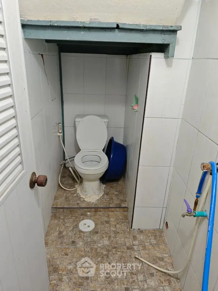 Compact bathroom with toilet and tiled flooring, featuring a unique layout.