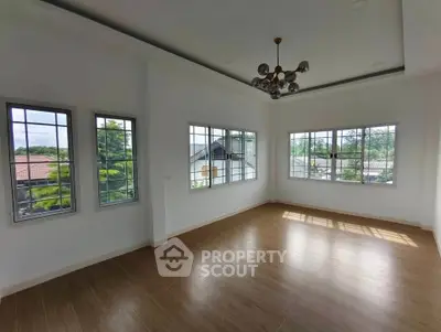 Spacious empty room with large windows and modern chandelier, offering abundant natural light and serene views.