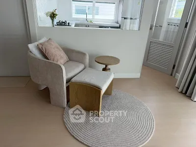 Cozy modern living space with stylish chair and ottoman, featuring a sleek kitchen view.